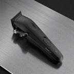 Black Tensor1 professional clipper resting on a brushed metal barber station counter with grooming products in the background, showcasing its matte finish and ergonomic design in a real barbershop setting.