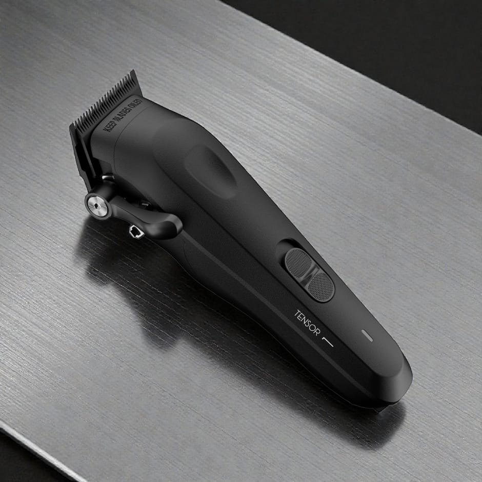 Black Tensor1 professional clipper resting on a brushed metal barber station counter with grooming products in the background, showcasing its matte finish and ergonomic design in a real barbershop setting.