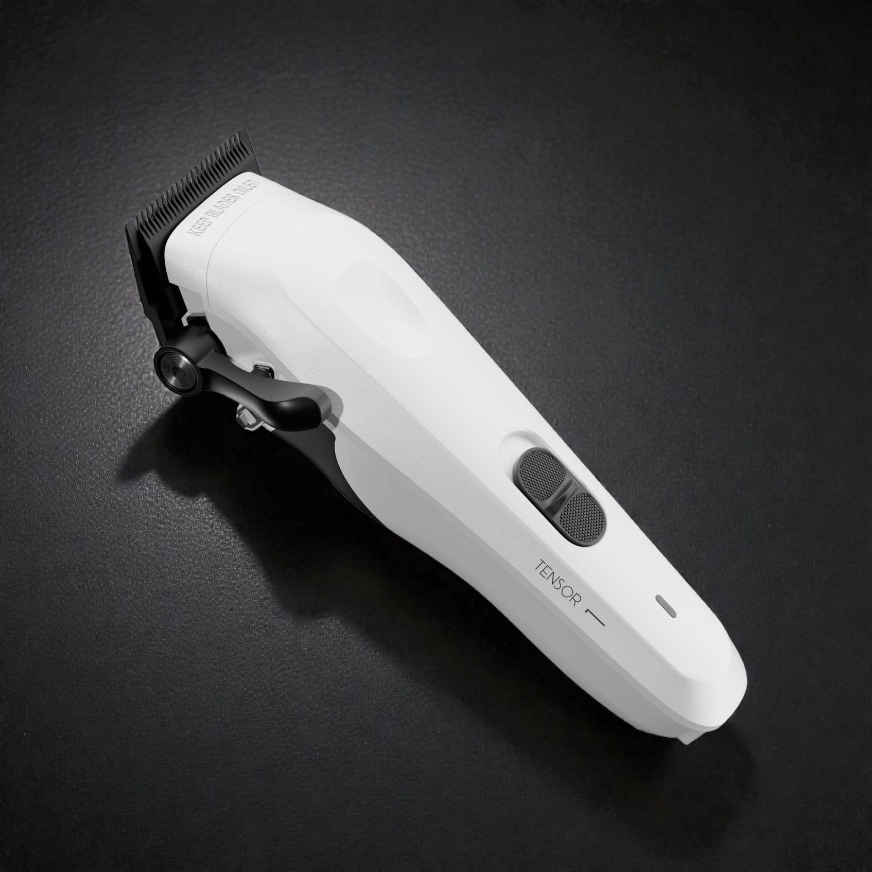Angled studio image of the white Tensor1 clipper on a dark textured surface, showcasing its clean modern design, ergonomic controls, and precision blade head.